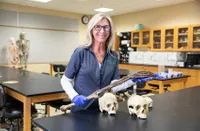 Barb Hanbury in lab with two skulls and a hand. 