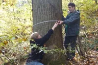 Two students using a piece of string to measure the width of the trunk of a tree 