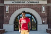 A York College student in a bright red shirt posing in front to Northside Commons 