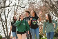 A group of five students talk and laugh as they walk across campus, 