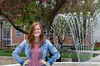 A YCP student posing in front of the campus fountain in a pink dress and blue jean jacket 