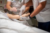 Nursing students checking pulse on sim lab doll.