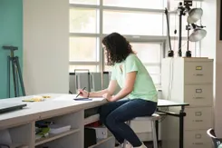 A graphic design student sits at a drafting desk and works