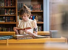 A student sits at a table in the library archives, reading through the aged pages of books and documents in front of her.