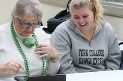 A student works with a resident in a nursing home to use an Ipad.