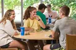 Three students talk and eat while sitting at a round table in the Johnson Dining Hall.