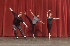Students dance on stage in front of red curtain in WPAC.
