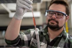 A student holds a pipette full of red liquid while wearing safety goggles and gloves in the lab.