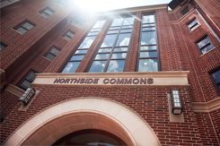 The front of a tall brick building with large windows and an archway entrance has signage reading Northside Commons