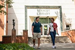 Two students walk side by side along the sidewalk in front of the Schmidt Library
