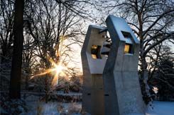 The chapel bell sits in front of a snow-covered scene, the sun rising in the background.