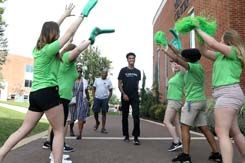 Orientation leaders in green t-shirts greet an incoming student and his family by waving green pom poms and foam fingers outside the Performing Arts Center.
