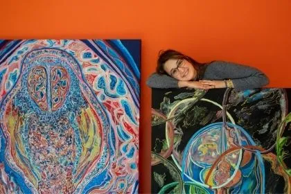 A Fine Art student posing with two of her colorful painting depicting what the mind looks like for those with neurological disorders 