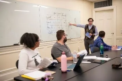 A professor at the college, Vinny Cannizzaro, teaching three students from a whiteboard in a classroom 