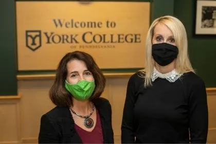 Two graduate business students posing for their picture in front of a Welcome to York College sign 