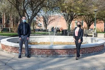 Two supply chain management students, Kylie Good and Luke Kessler, posing in front of the campus fountain in their business suits 