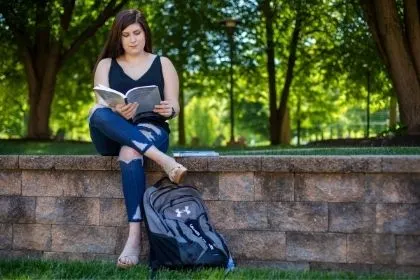 A Biology student sitting on the edge in the amphitheater reading a behavioral research book 