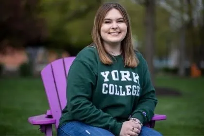 A student sitting on a purple Adirondack chair on main campus lawn 