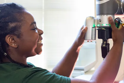 A student smiles as she adjusts a mechanical cobot in the MRG Labs 