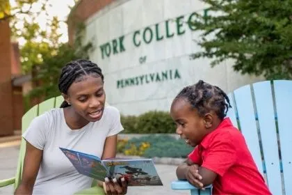 A Criminal Justice student reading her son a book in front of a York College of PA sign 