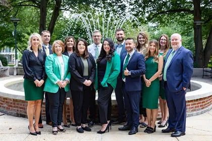 A group of 13 admissions professionals pose together for a photo in front of the campus fountain. 