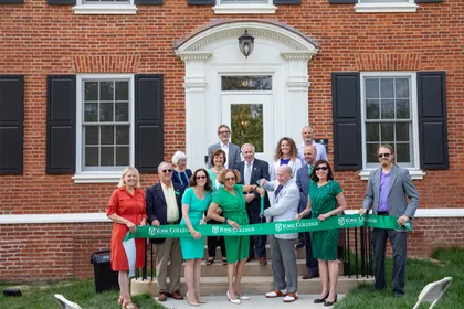 A group of 14 stakeholders from YCP and the community gather on the steps of the Diehl House to cut a large ribbon emblazoned with the York College of Pennsylvania logo. 