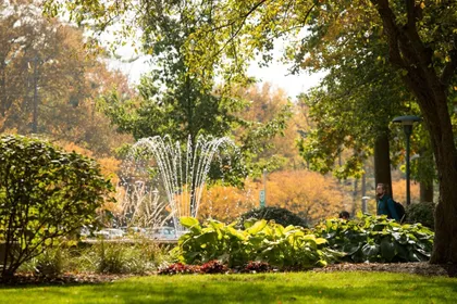 The beautiful Campus fountain turned on in the middle of fall, surrounded by beautiful orange leaves 
