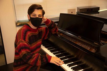 Grant at grand piano with face mask on