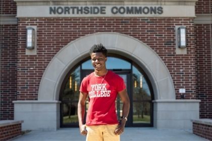 A York College student in a bright red shirt posing in front to Northside Commons