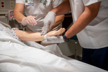 Nursing students checking pulse on sim lab doll.