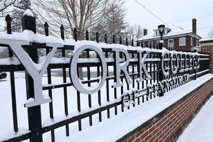 Metal letters spell York College of Pennsylvania along a wrought iron fence, covered in snow.