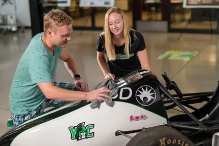 Two students look at a YCP-branded stock car in the Kinsley Engineering building 