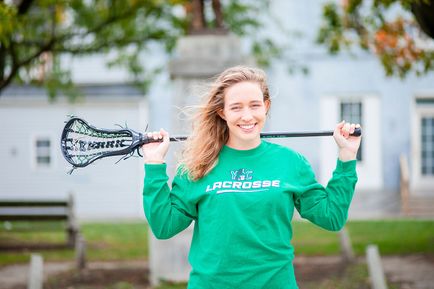 Rachael Huebler stands holding a lacrosse stick on her shoulders.
