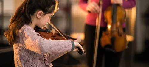 A young girl around ten years old plays a violin during a lesson as her instructor stands nearby, violin at rest.