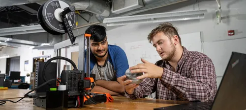 Two students examine a 3D printer in the engineering lab.
