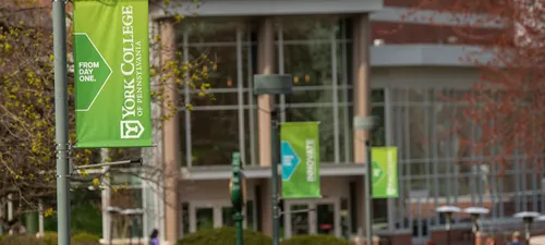 Green York College banners adorn the flag poles along the sidewalk leading up to the glass entryway of the Performing Arts Center