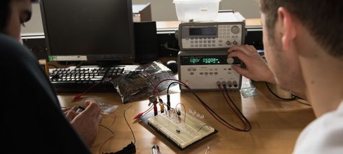 Two students work on a circuit with equipment in the engineering lab
