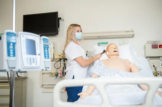 A nursing student holds an otoscope to a mannequin's ear in the simulation lab