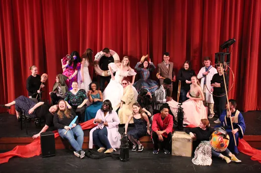 A group of theatre students stands in costume on stage.