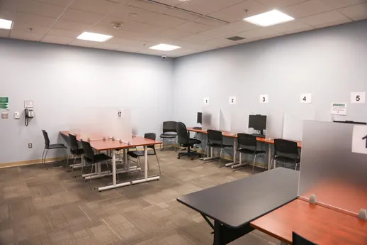 A computer lab in the Testing Center shows rows of tables with desktop computers and frosted glass dividers between seating areas.