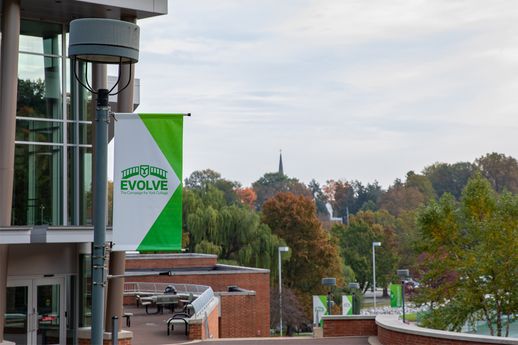 An autumn shot of campus shows the Evolve campaign flag flying in front of the WPAC with fall foliage in the background