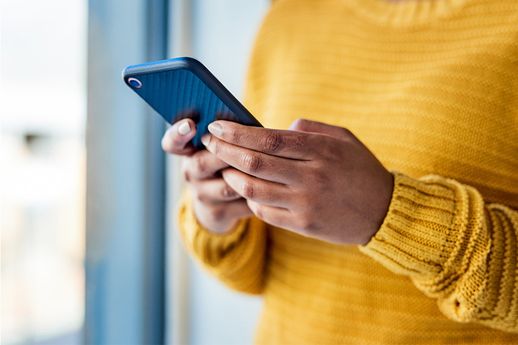 A close-up image shows a pair of hands holding a mobile phone. A cozy yellow sweater is visible but we cannot see the face of the user.