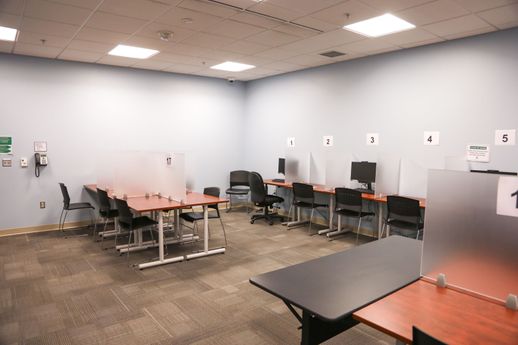 A computer lab in the Testing Center shows rows of tables with desktop computers and frosted glass dividers between seating areas.