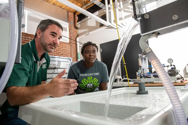A student and faculty member watch as water pours into a sink from machinery in the engineering lab