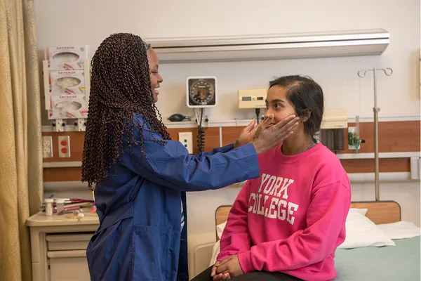 A nursing student feels the throat of a patient in a simulated clinical setting.