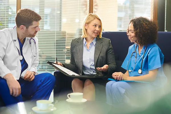 a professional woman speaks with two medical professionals dressed in scrubs