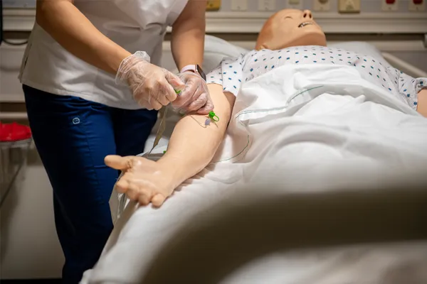 A nursing student practices inserting an IV on a mannequin in the nursing simulation lab