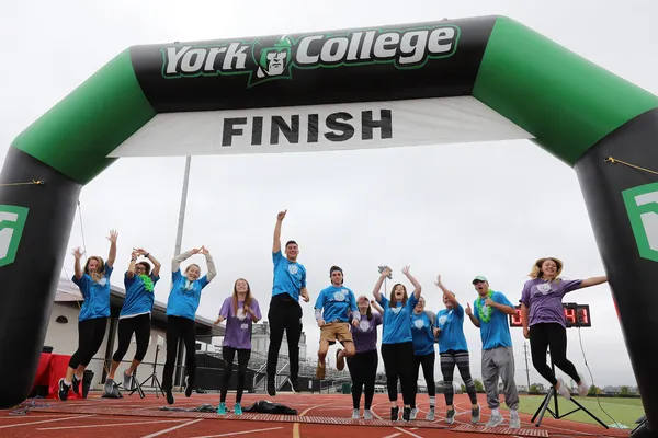 A group of alumni jump victoriously at the Fun Run finish line