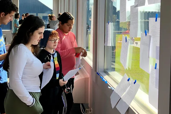 A small group of students look at papers taped to a window during a design thinking exercise.