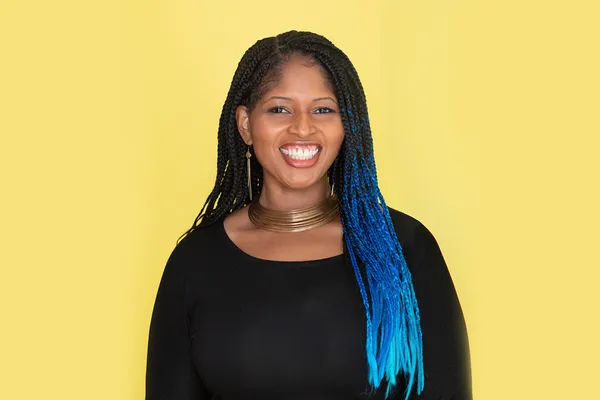 Professional photo of Mecca Jamilah Sullivan, standing against a yellow backdrop.